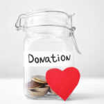 Glass jar with coins and red heart on table. Concept of donations